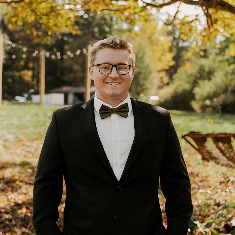 Man wearing a black and white suit and black glasses posing outside