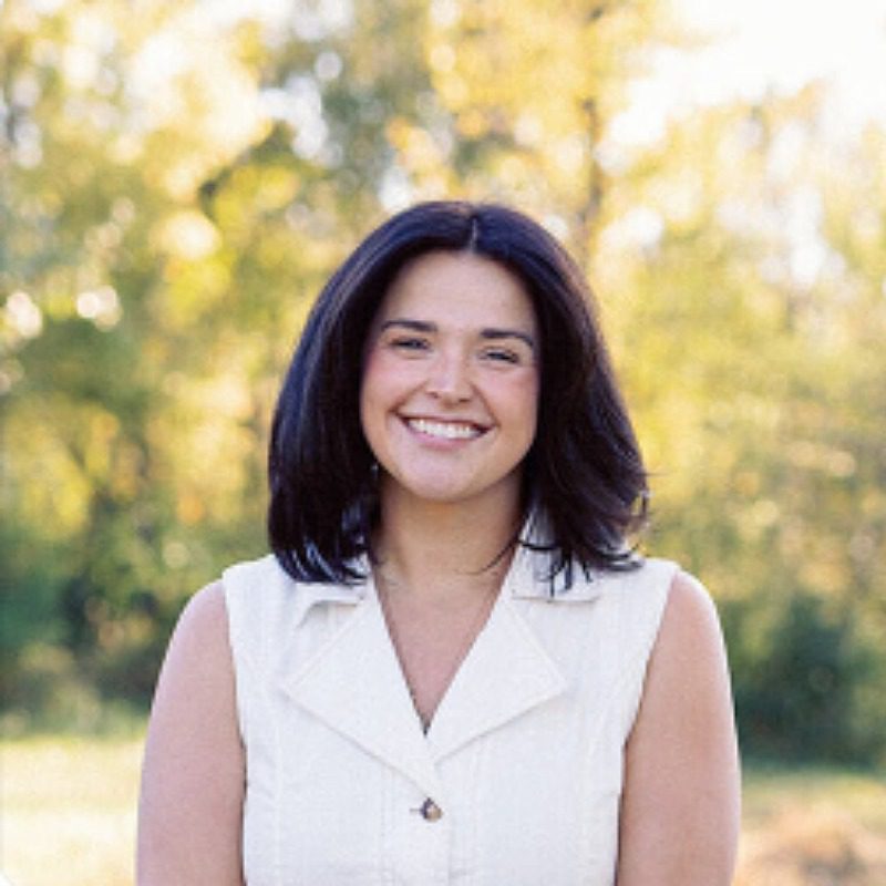female with shoulder length dark hair and white v-neck collared sleeveless shirt