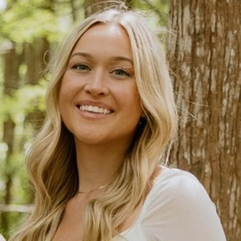 Madison H - female with long blonde wavy hair wearing a white blouse standing in front of a tree