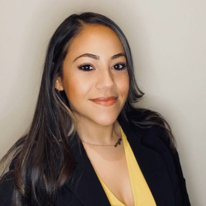 Lori Peraza Soles female with long dark hair wearing a yellow top and black blazer